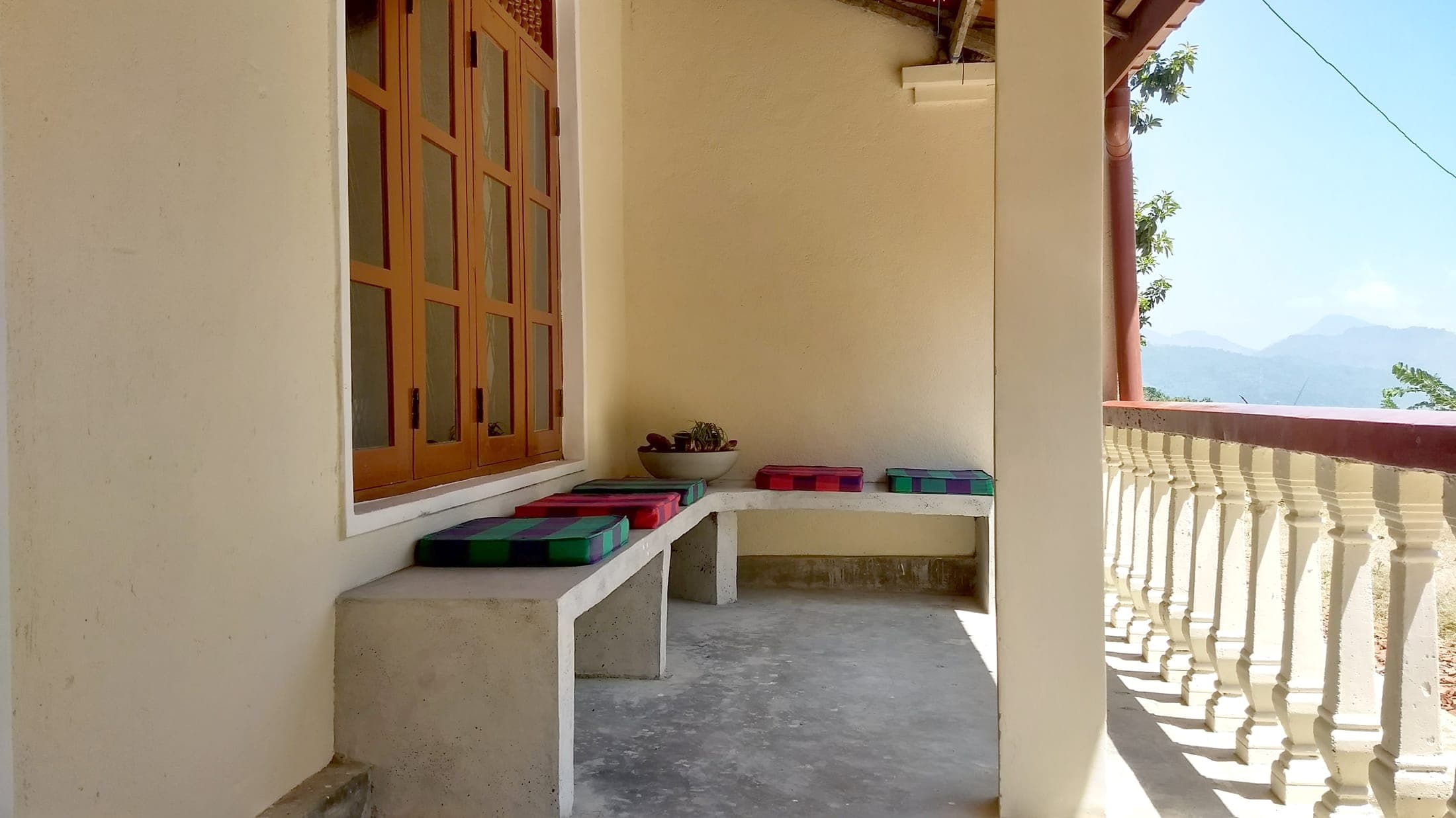 Shaded front veranda with a built-in bench, colourful cushions and a view to the hills